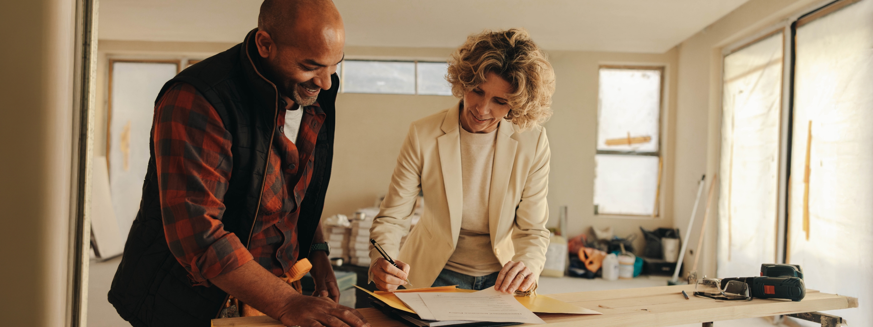 A homeowner signing a change order on site while her contractor looks on, both smiling